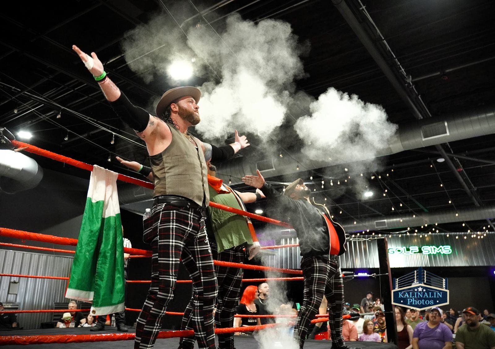 Wrestlers celebrate in the ring through a cloud of smoke